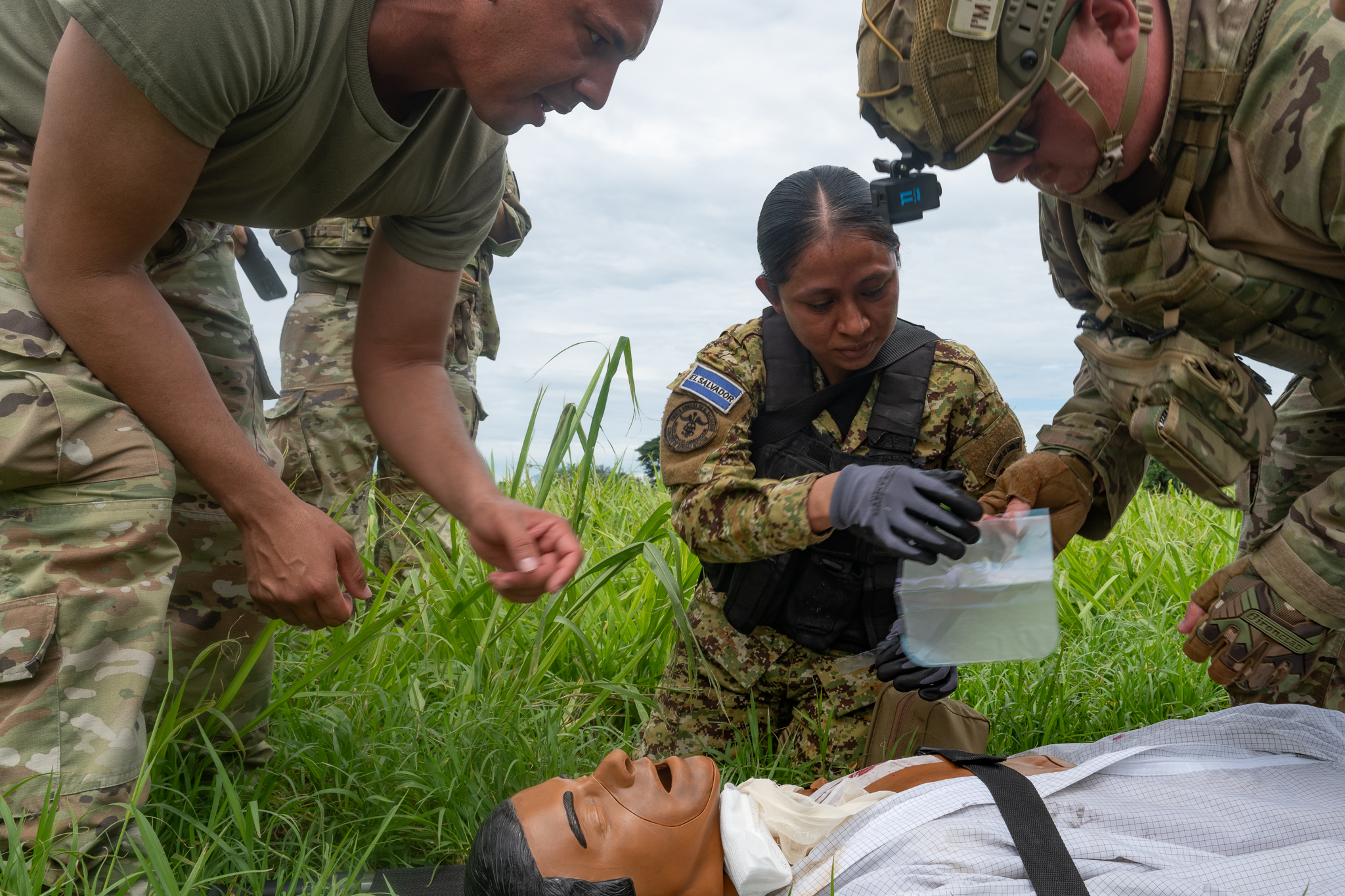 U.S. Air Force Tech. Sgt. John Nazario (left) and Capt. Samuel Hendricks assist an El Salvador Primera Brigada Aérea member with applying a seal to a sucking chest wound to a medical training mannequin.